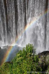 A rainbow is seen in the background of a waterfall.