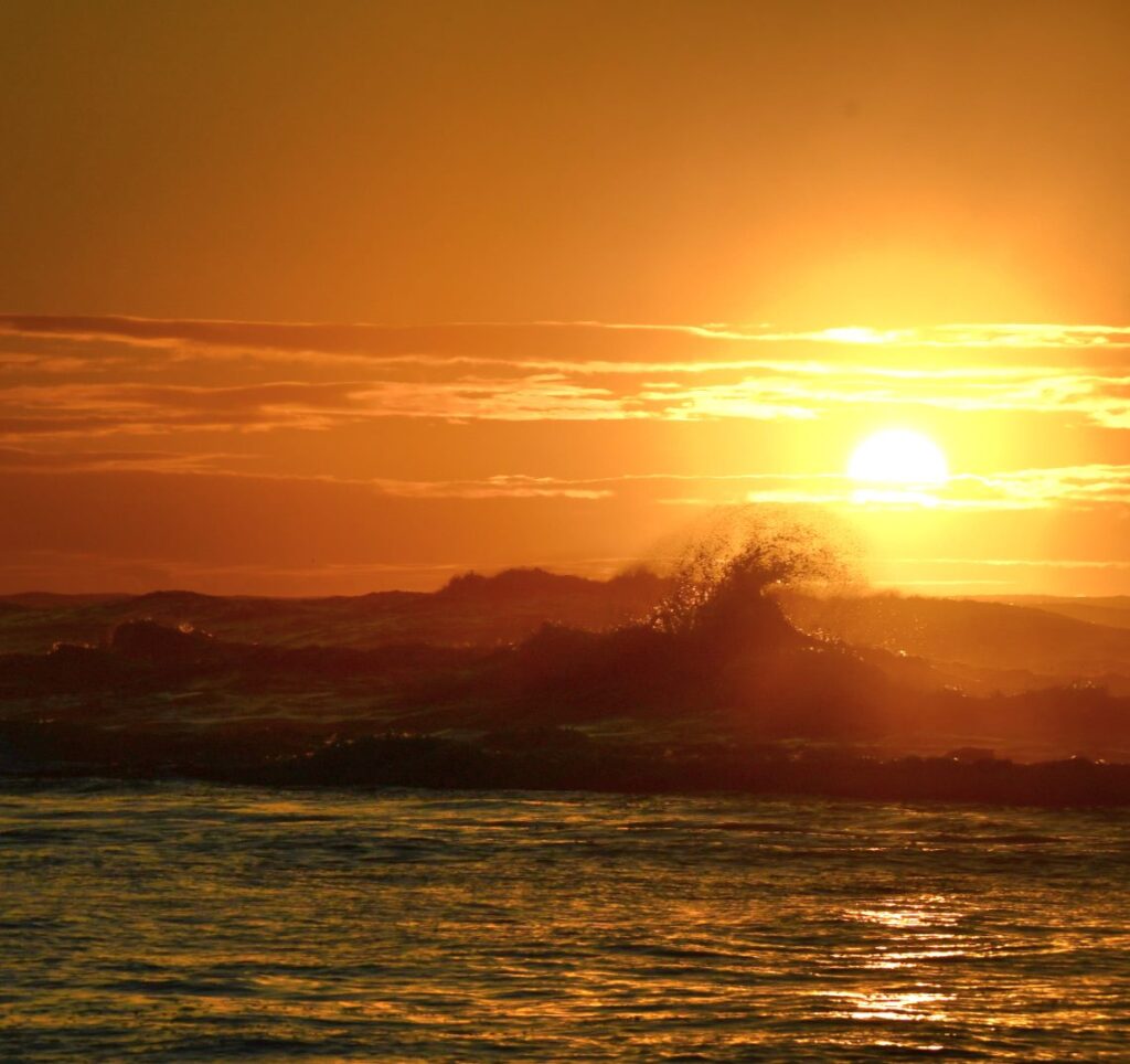 A sunset over the ocean with waves crashing in.