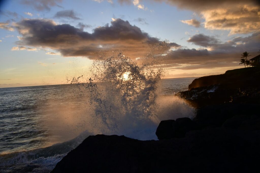 A wave crashing on the rocks at sunset.