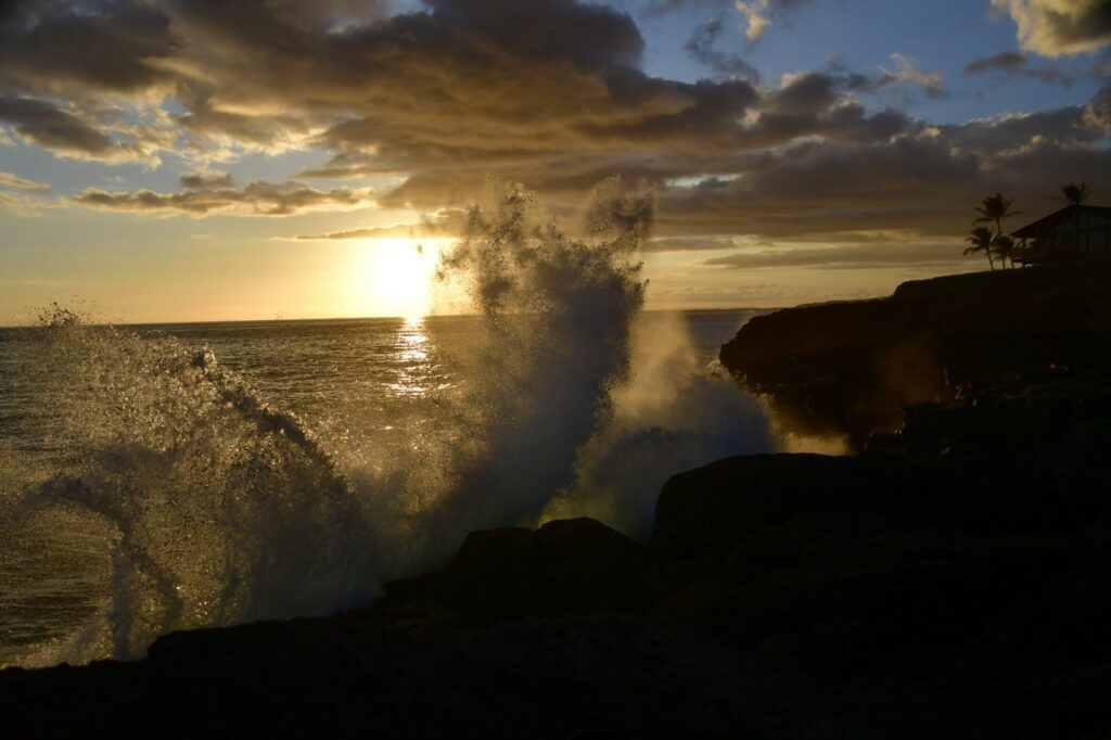 A wave crashing on the rocks at sunset.