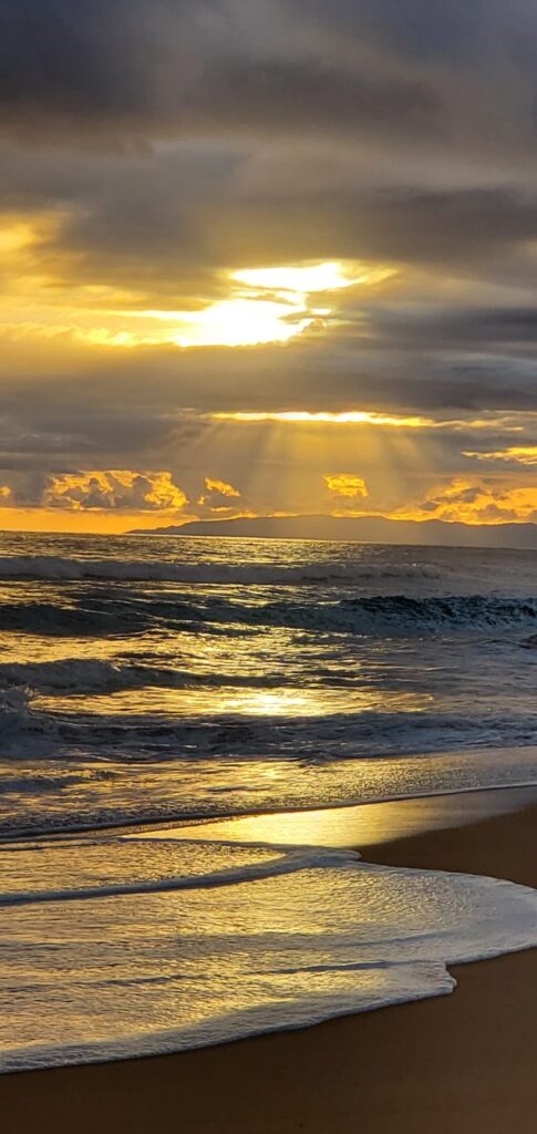 A sunset over the ocean with sun shining through clouds.